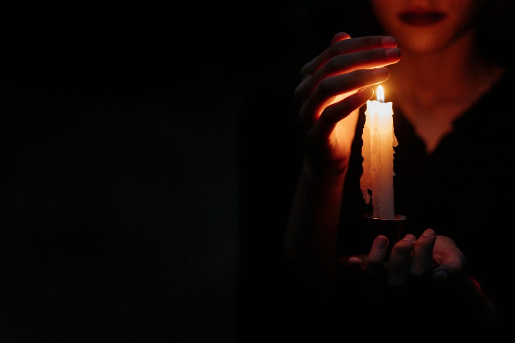 Close-up of a person in the dark holding a single lit candle, creating a moody atmosphere.