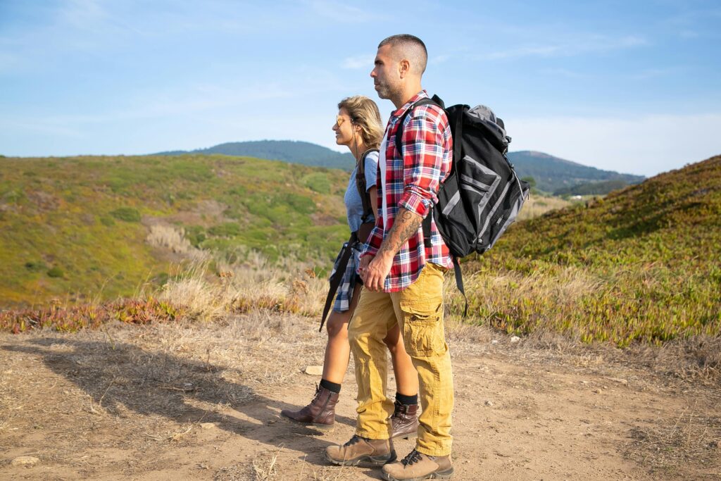 Couple hiking in Portugal's lush landscape with backpacks under a clear blue sky.